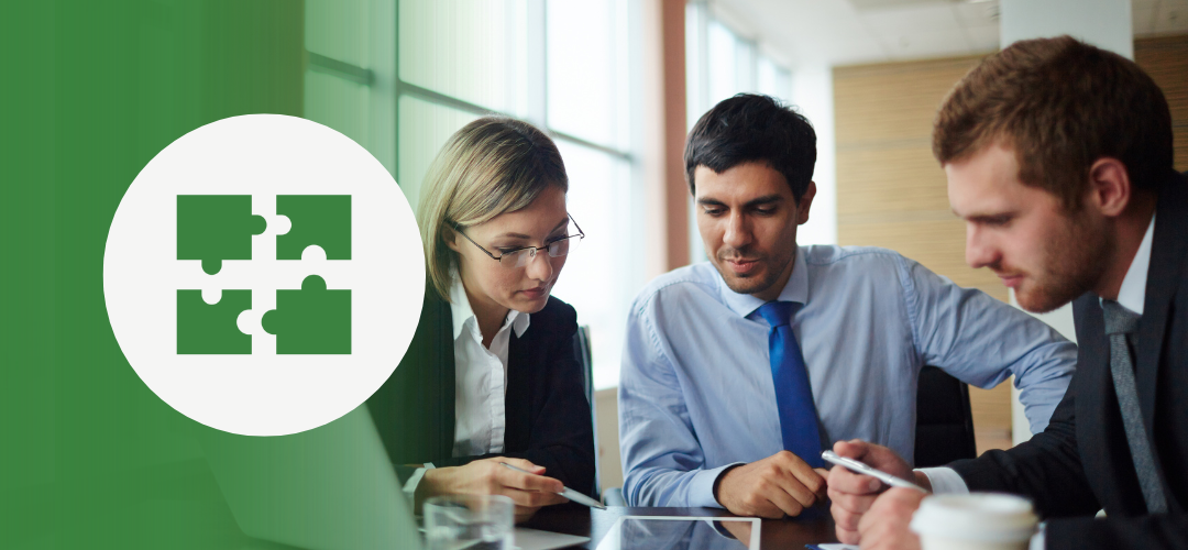 Three professionals (two men and one woman) in formal attire sit around a table reviewing documents or a tablet in a modern office. On the left, a green overlay shows a white circle containing four interlocking puzzle pieces—symbolizing collaboration, teamwork, or integrated solutions.