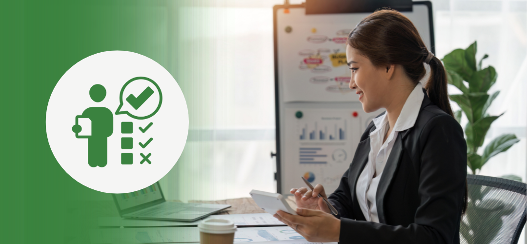 A businesswoman in a suit smiles while working at her desk with a laptop, tablet, and charts. Behind her is a whiteboard with strategy diagrams. On the left side of the image, a green overlay features a white icon of a person holding a clipboard and a checklist with a check mark in a speech bubble—symbolizing evaluation or performance tracking.