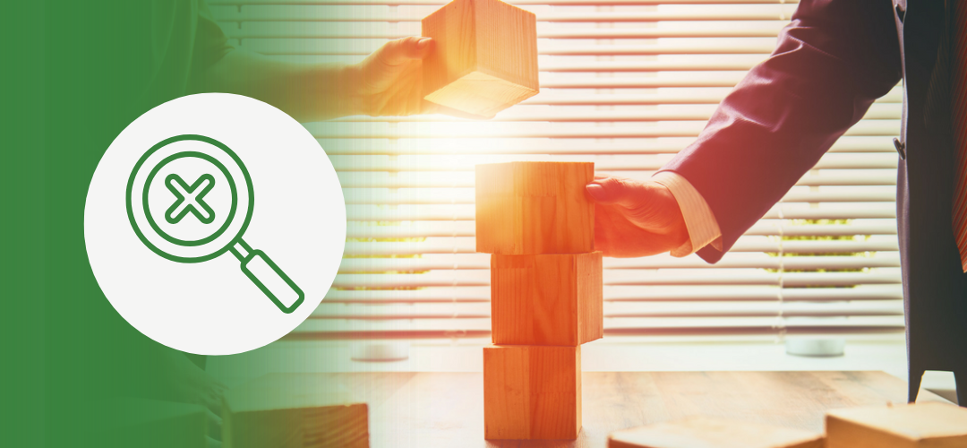 A businessperson in a suit places a wooden block atop a small tower of other wooden blocks, symbolizing strategic planning or decision-making. On the left, a green overlay features a white circle with an icon of a magnifying glass over an X—symbolizing mistake identification or misalignment.