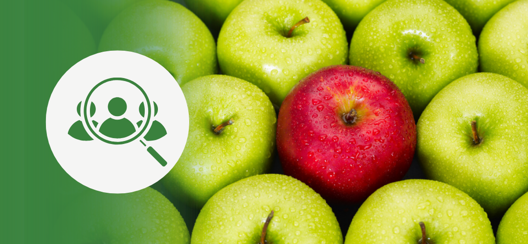 Close-up of apples with one red apple standing out among many green apples. On the left, a green overlay displays a white icon of a magnifying glass over a person’s head—symbolizing candidate search or identifying the right hire.